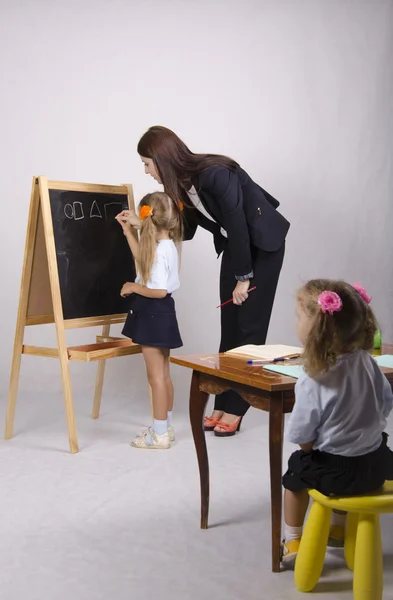 Op het schoolbord meisje met een tutor vormen tekenen, een ander meisje zitten aan de tafel — Stockfoto