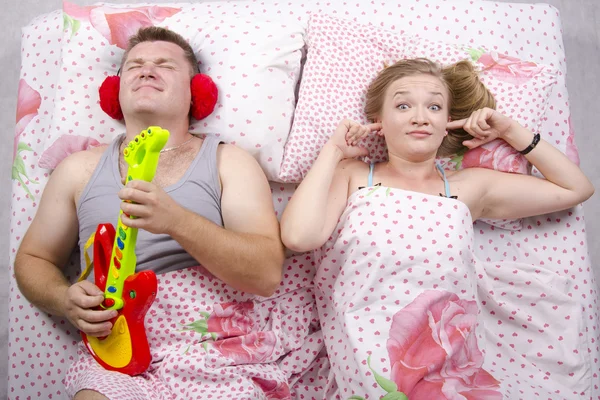 The couple in the bed-husband plays guitar, wife covered her fingers in his ears — Stock Photo, Image