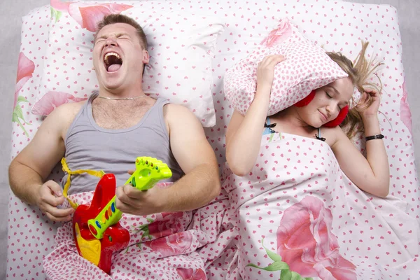 The couple in the bed-husband plays guitar, wife covered her pillow — Stock Photo, Image