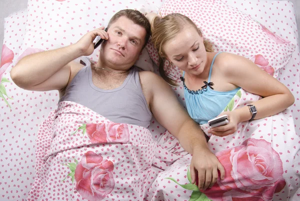 躺在床上的电话上谈了对年轻夫妇 — 图库照片