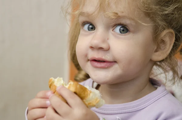 La petite fille avec enthousiasme et mange un rouleau avec plaisir — Photo