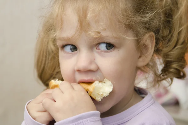 La petite fille avec enthousiasme et mange un rouleau avec plaisir — Photo