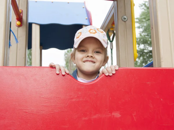 A girl peeks out from behind the shield playing on the Playground — Stock Photo, Image