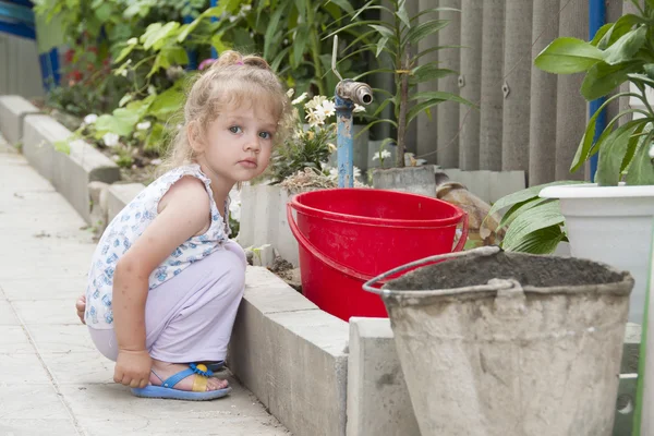 La fille assise dans le jardin à côté du seau et de la grue — Photo