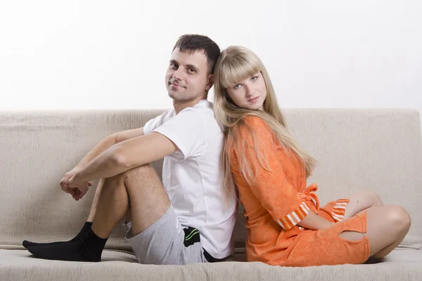 Couple sitting on the couch with his back to each other and looking in the frame — Stock Photo, Image