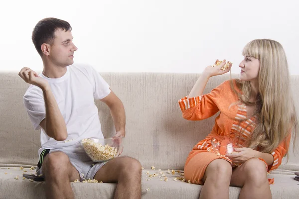 Mladý pár, sedí na gauči a hodil navzájem popcorn — Stock fotografie
