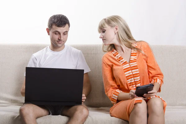 Le gars avec l'ordinateur portable assis sur le canapé, la fille avec la tablette regarde dans son ordinateur portable — Photo