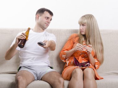 The pair on the couch. He looks drinking beer, she looks at him reproachfully clipart