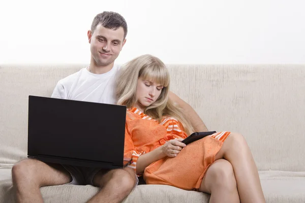 Um menino e uma menina sentados no sofá com o laptop e tablet — Fotografia de Stock