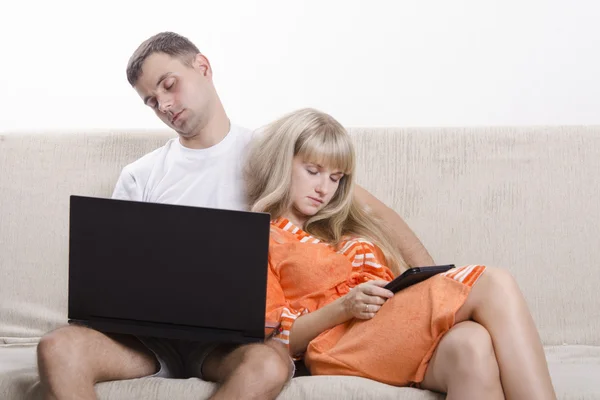 Ragazzo e ragazza addormentati, seduti sul divano con il computer portatile e tablet — Foto Stock