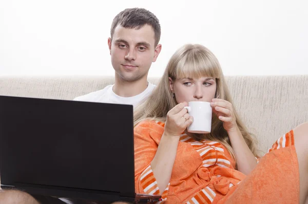 The guy sitting with his laptop on the couch, sitting next to a girl with a Cup of tea Stock Image