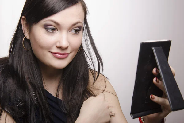 A beautiful young girl looks in the mirror after applying makeup — Stock Photo, Image