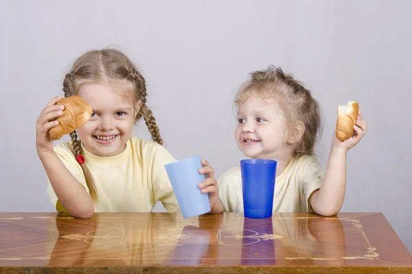 Dos niños comen un panecillo en la mesa — Foto de Stock