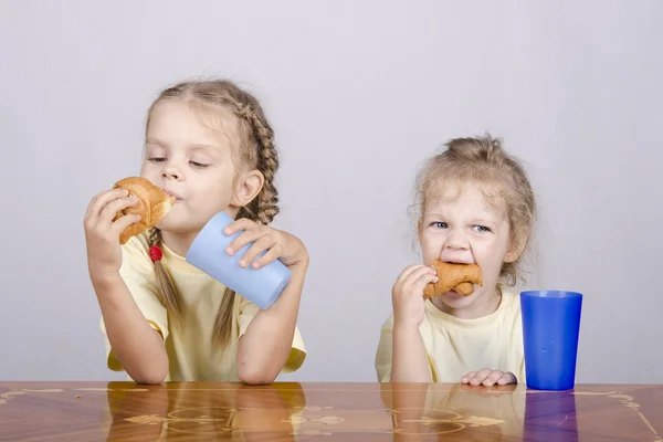 Dos niños comen un panecillo en la mesa — Foto de Stock