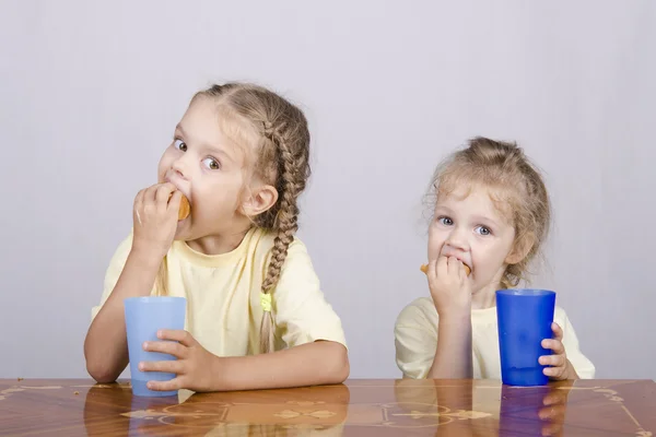 Dos niños comen un panecillo en la mesa — Foto de Stock