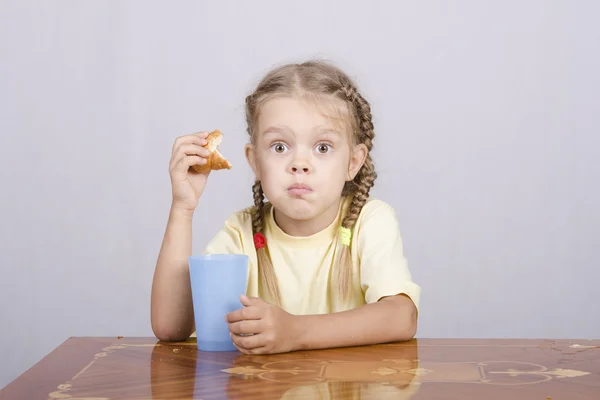 Menina comendo um queque com suco na mesa — Fotografia de Stock