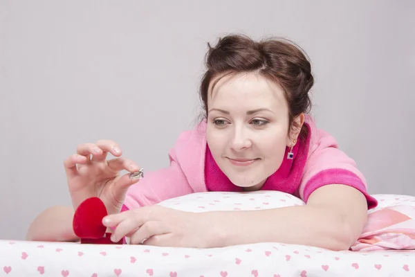 Chica sostiene un anillo de regalo, acostado en la cama — Foto de Stock