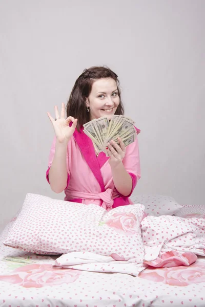 Young girl sitting in bed with a bundle of money — Stock Photo, Image