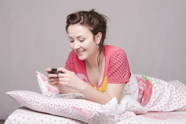 Happy girl writes SMS in bed — Stock Photo, Image