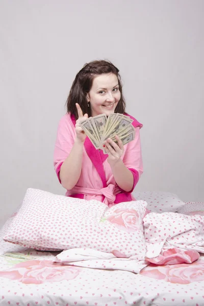 Happy girl sitting in bed with a bundle of money — Stock Photo, Image