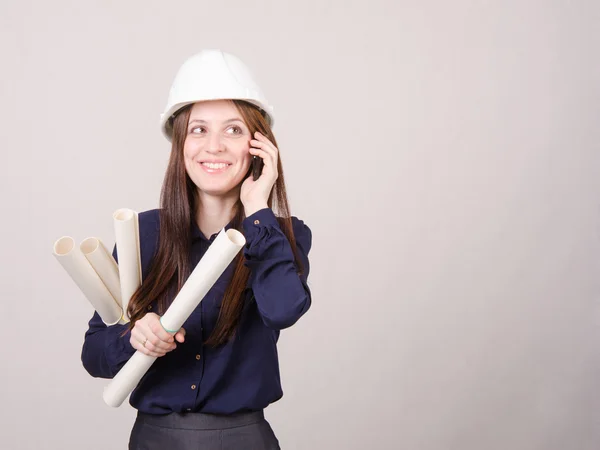 Young woman talking on phone with blueprints in hand — Stock Photo, Image