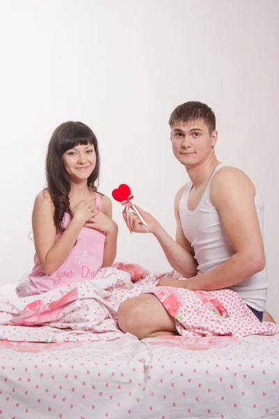 Young man gives heart beautiful girl in bed — Stock Photo, Image