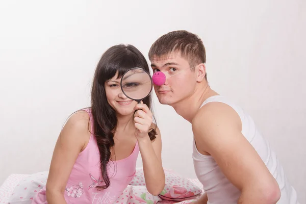 Girl with magnifying glass, guy clown nose — Stock Photo, Image