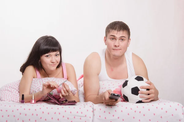 Мужчина смотрит футбол по телевизору, девушка-маникюр занимается в постели — стоковое фото