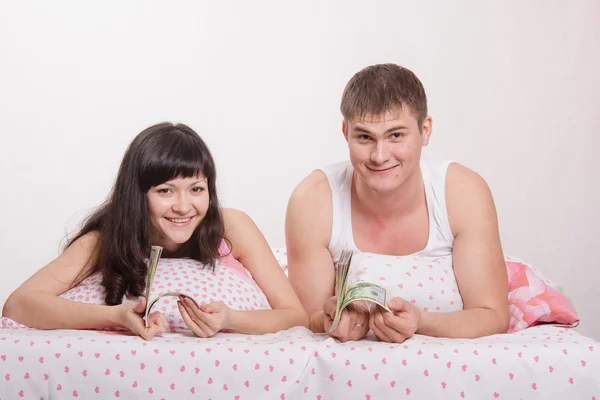 Girl and guy with a wad of dollars in bed — Stock Photo, Image