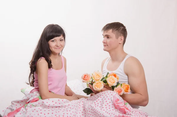 Chica recibe flores de un chico sentado en la cama —  Fotos de Stock