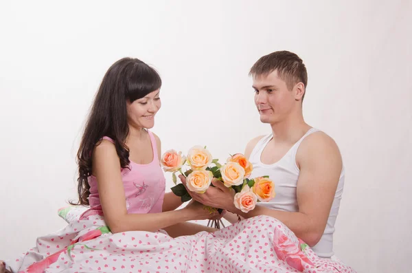 Chica recibe flores de chico sentado en la cama —  Fotos de Stock