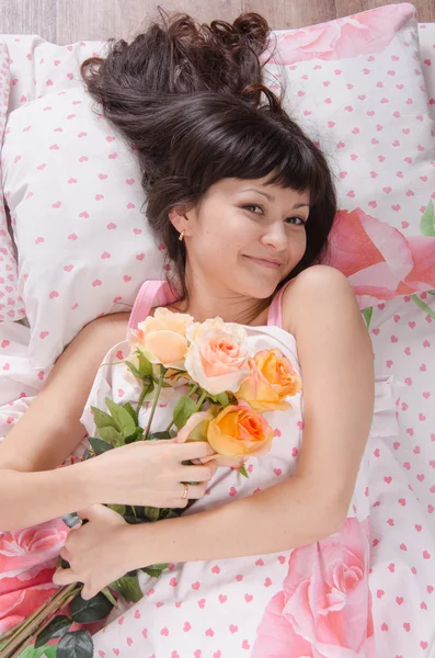 Mooi meisje liggend in bed met boeket rozen — Stockfoto