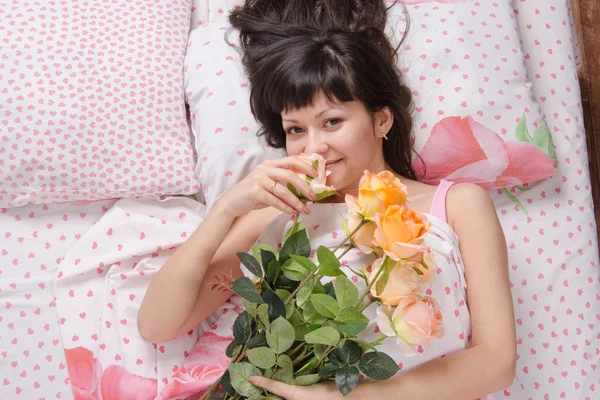 Beautiful girl enjoying scent of flowers in bed — Stock Photo, Image