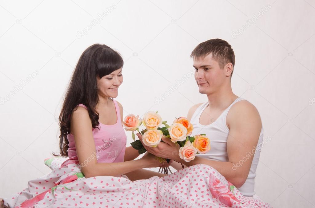 Girl receives flowers from guy sitting in bed
