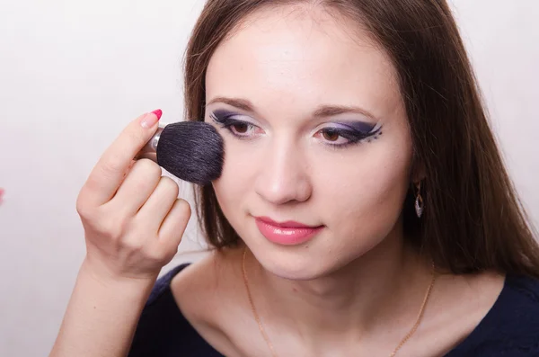 Beautiful young girl applying makeup on face — Stock Photo, Image