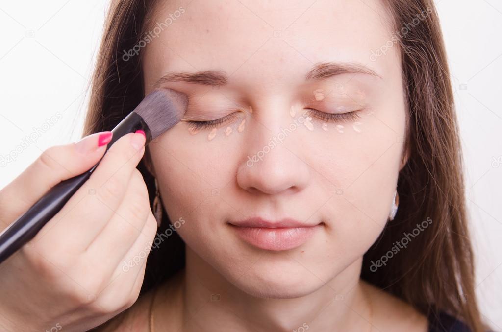 Makeup artist is shaded brush concealer on eyelids model