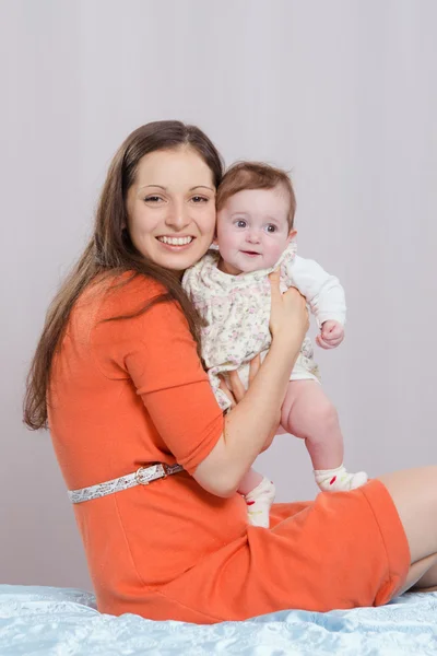 Mãe com uma filha de seis meses sentada na cama — Fotografia de Stock