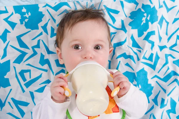 Baby lying in crib and drinking milk from a bottle — Stock Photo, Image