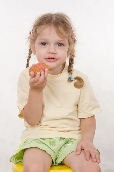 Девушка ест булочку сидя на стуле — стоковое фото
