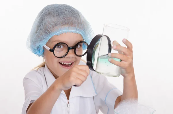 Meisje scheikundige onderzoekt kolf onder een vergrootglas — Stockfoto