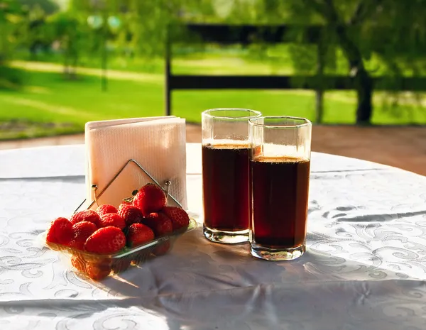 Two glasses of coda drink and a pile of strawberries on the table in a sunny day