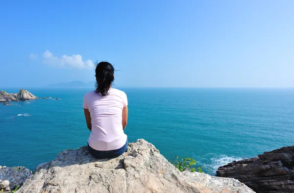 Atrás de la mujer sentarse en la roca junto al mar — Foto de Stock