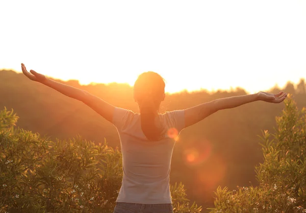 Благодарная женщина с распростертыми объятиями к восходу солнца — стоковое фото