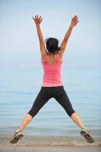 Achterkant van gelukkig vrouw springen kust strand — Stockfoto