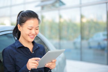 güzel Asyalı işkadını arabanın üzerine eğilerek dijital tablet kullanımı
