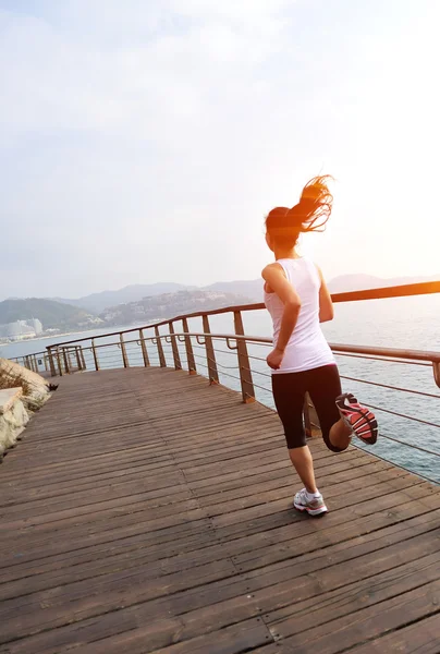 Mujer corriendo por sendero de madera junto al mar —  Fotos de Stock