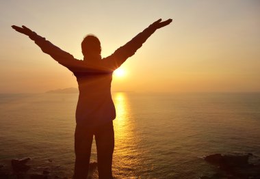 Woman open arms to sunrise at sea clipart