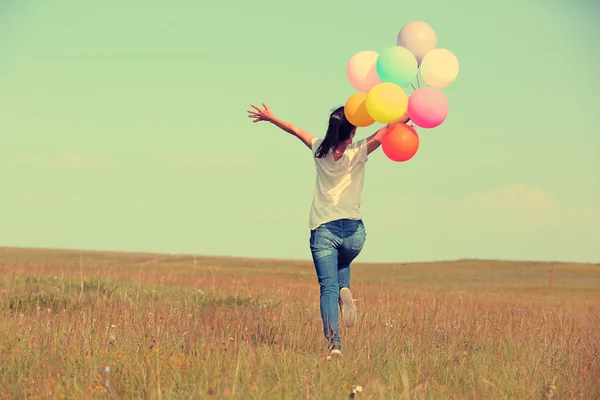 Junge Frau läuft mit bunten Luftballons — Stockfoto