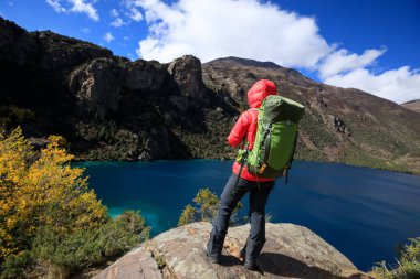 Sırt çantalı kadın akıllı telefon kullanarak güzel bir kış zirvesinde uçurumun kenarında fotoğraf çekiyor.