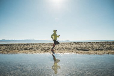 Kışın göl kenarında koşan koşucu kadın.